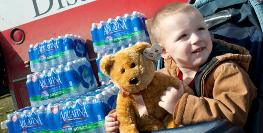 Toddler holding a Red Cross teddy bear in front of an emergency response vehicle 